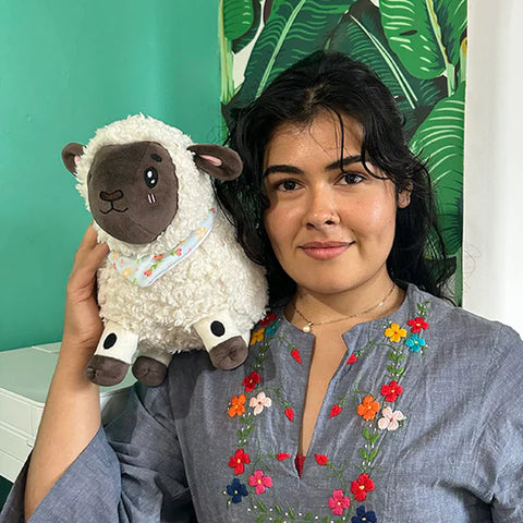 Image shows a woman holding the stuffed lamb on her shoulder. It is roughly the size of her head.