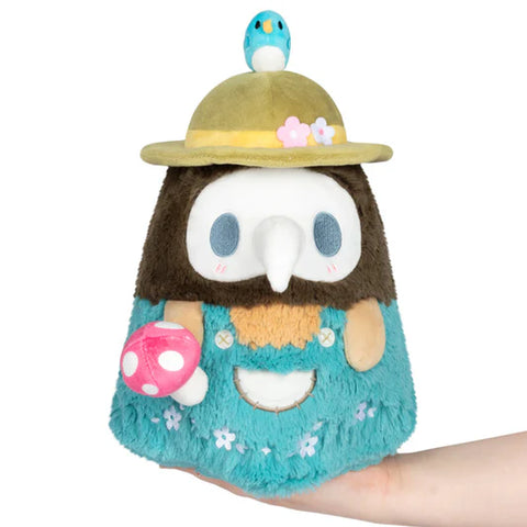 Image shows a stuffed plague doctor wearing turquoise overalls and a wide brim hat, holding a mushroom.