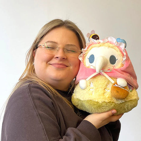Image shows a woman holding the stuffed spring mushroom themed plague nurse. It is slightly larger than her head.