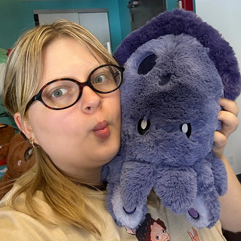 A woman holds the purple plush squid toy. It is slightly larger than her head.