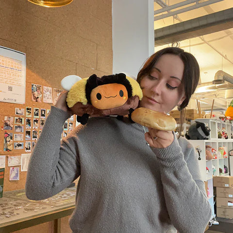 A woman holds the plush doughnut bee up to her face. It is slightly larger than her head.