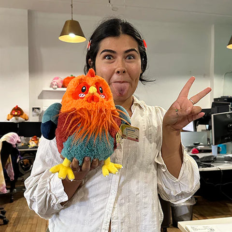 A woman holds the plush rooster near her face. It is slightly larger than her head.