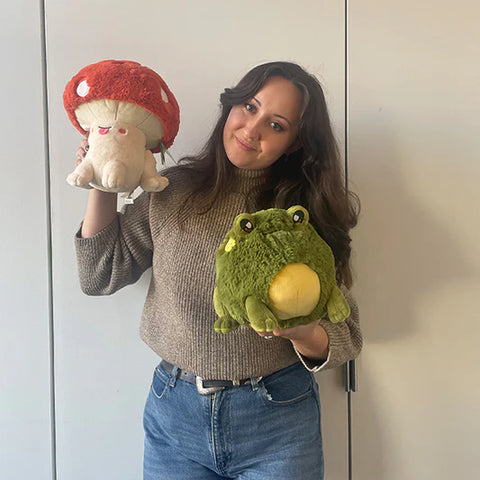 A woman holds the plush toadstool near her face. It is slightly larger than her head.