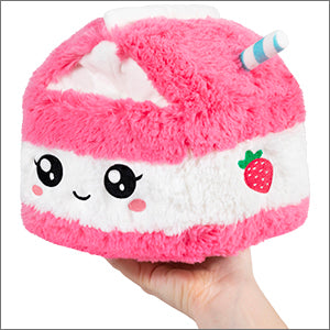 A plush toy resembling a pink strawberry milk carton with a smiling face and a strawberry decoration on the side, held in someone's hand