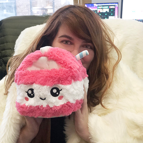 A woman holds the plush strawberry milk carton near her face. It is slightly larger than her head.