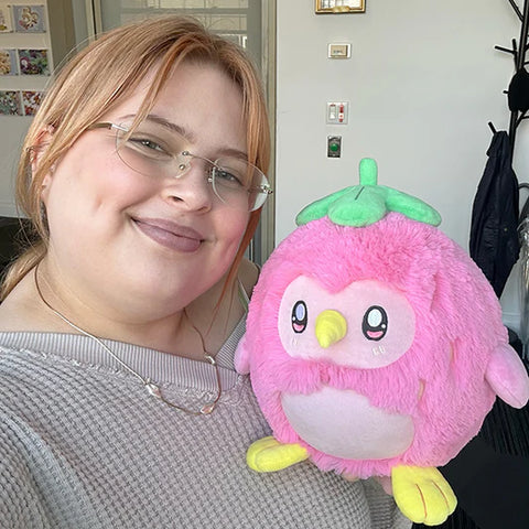 Image shows a woman holding the stuffed strawberry penguin. It is about the size of her head.