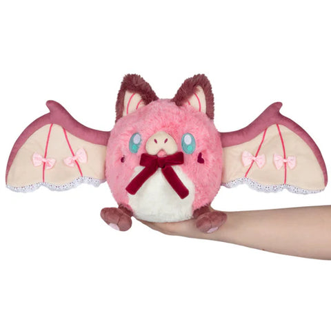 Image shows a pink and maroon stuffed bat. Its wings are lined with lace and bows and it has a bow at its throat.