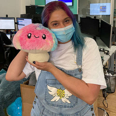 A woman holds the plush tie dye mushroom near her face. It is slightly larger than her head.
