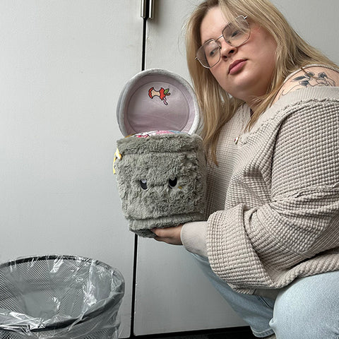 Image shows a woman holding the stuffed trash can over a real trash can. It is slightly larger than her head.