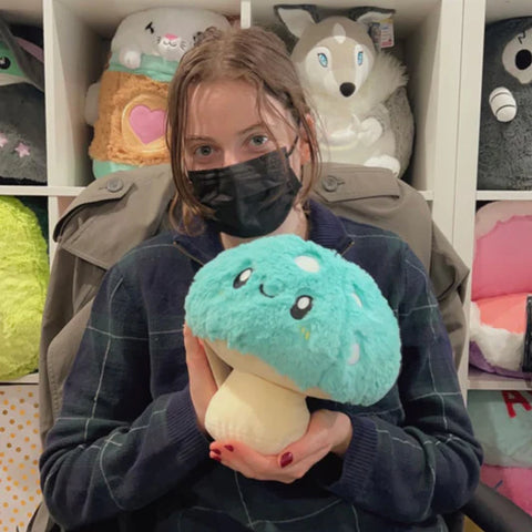 A woman holds the plush mushroom near her face. It is slightly larger than her head.