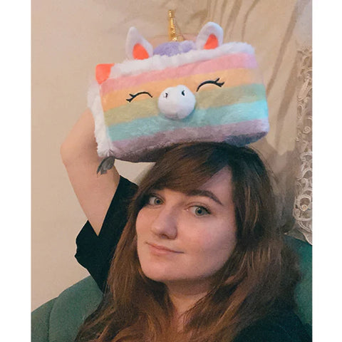 A woman holds the plush unicorn cake on her head. It is slightly larger than her head.