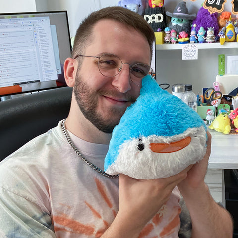 Image shows a man holding the stuffed whale shark up to his face. It is approximately the size of his head.