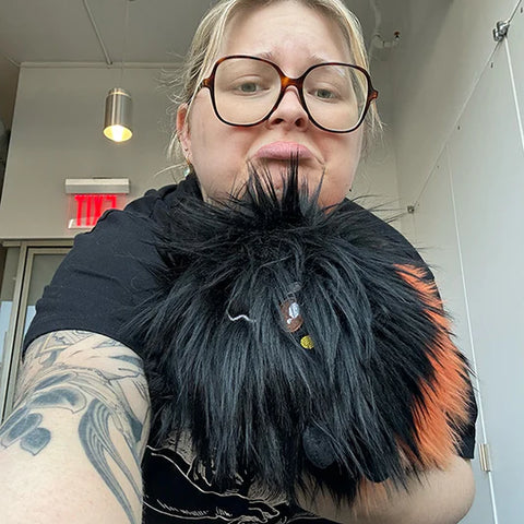 Image shows a woman holding the stuffed wooly caterpillar. It is slightly larger than her head.