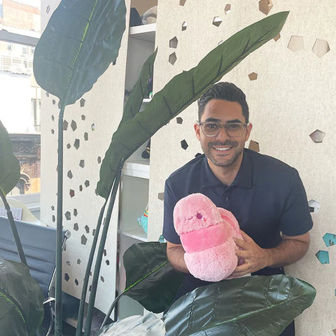 Image shows a man holding the stuffed pink worm. It is slightly larger than his head.