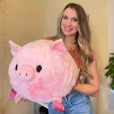 A woman holds the plush pig near her body. It is about the size of her torso.