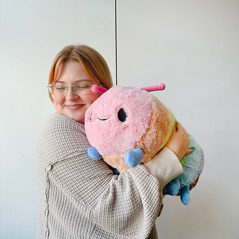 Image shows a woman hugging the pastel rainbow caterpillar. It is approximately the length of her torso.