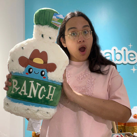 A woman holds the plush ranch dressing. It is about the size of her torso.