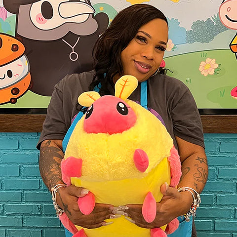 A woman holds the plush rosy maple moth. It is about the size of her torso.