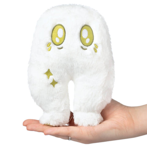 Small white plush toy with green eyes held in a hand against a white background