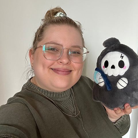 A woman holds the plush reaper near her face. It is slightly smaller than her head.