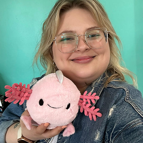 A woman holds the plush baby axolotl. It is slightly smaller than her head.