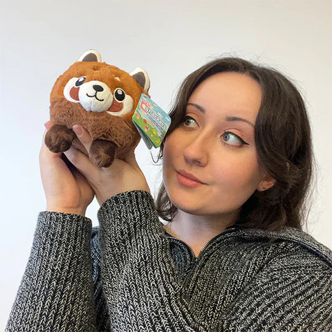 Image shows a woman holding the stuffed red panda up to her face. It is smaller than her head.