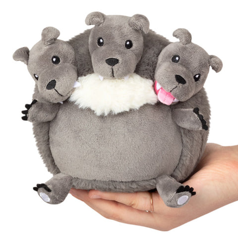 A plush toy resembling a creature with three dog heads, primarily in gray color, held in a person's hand.