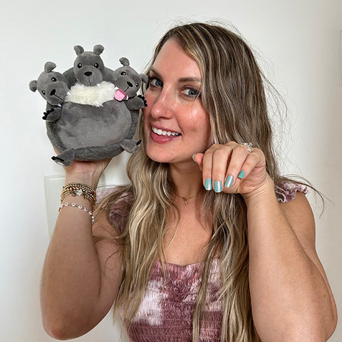 A woman holds the plush Cerberus near her face. It is slightly smaller than her head.