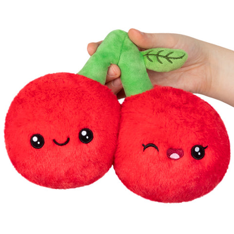 A plush toy resembling two cherries with faces, held in a person's hand.