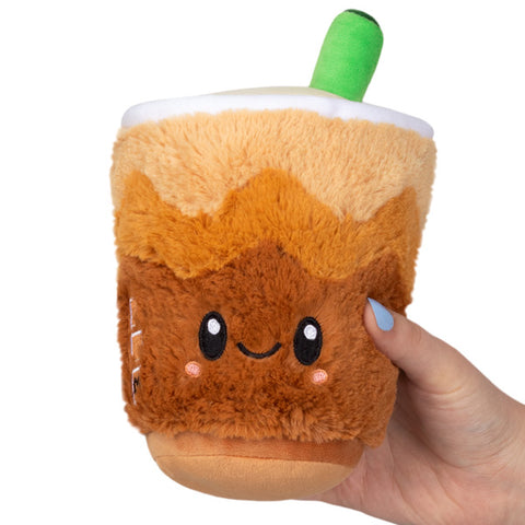 A plush toy resembling a cup of cold brew coffee with a smiling face, held in a person's hand.