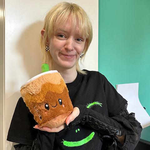 A woman holds the plush cold brew near her face. It is slightly smaller than her head.
