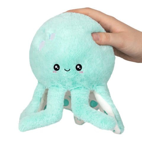 A plush toy resembling a mint-colored octopus with a cute face and cartoonish details, held by someone's hand