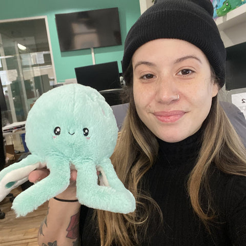 A woman holds the plush mint octopus near her face. It is slightly smaller than her head.
