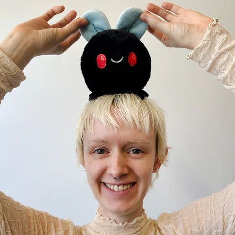 A woman holds the stuffed fly on top of her head. It is slightly smaller than her face.