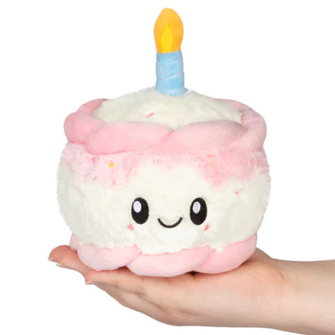Plush toy shaped like a birthday cake with a candle held in a hand on a white background