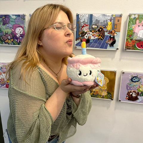 A woman holding the stuffed birthday cake. She is pretending to blow out the candle.