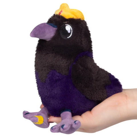 Image shows a stuffed raven in an adult's palm. He wears a crown and a ring on one toe.