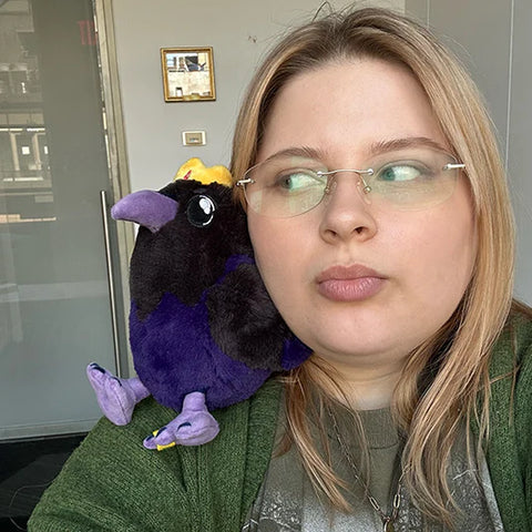 Image shows a woman with the stuffed king raven on her shoulder. It is slightly smaller than her head.