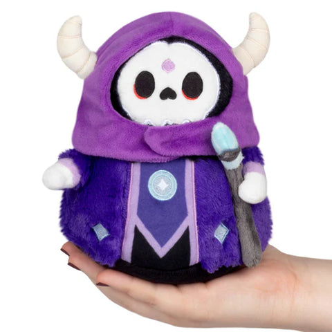 A Lich dressed in purple. It has horns and is holding a scepter. It is being held in an adult's palm.