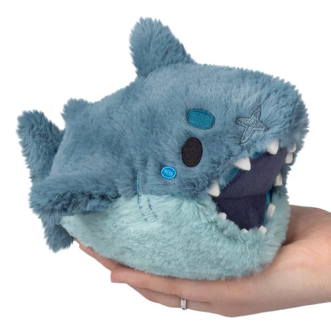 Blue plush megalodon shark toy held in a hand against a white background