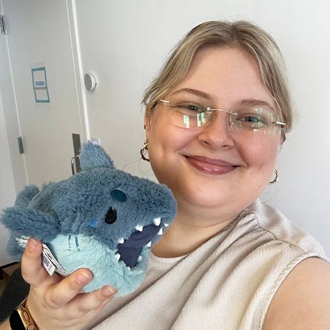 Woman holding the stuffed megalodon shark. It is slightly smaller than her head.
