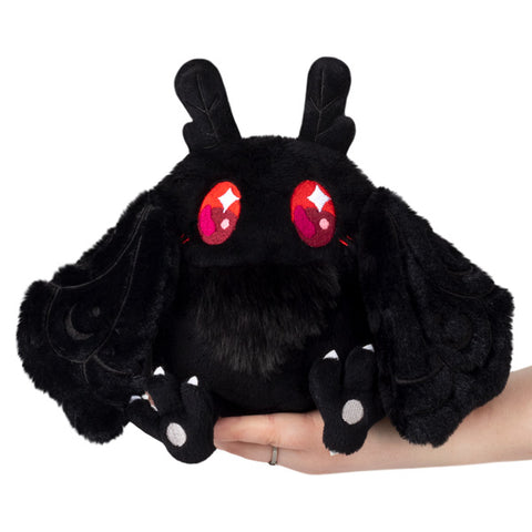 A plush toy resembling a black moth with red eyes, designed to look cuddly and soft, held in someone's hand.