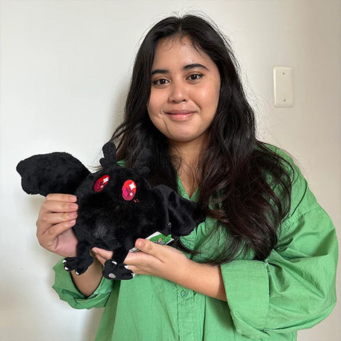 A woman holds the plush baby mothman. It is slightly smaller than her head.