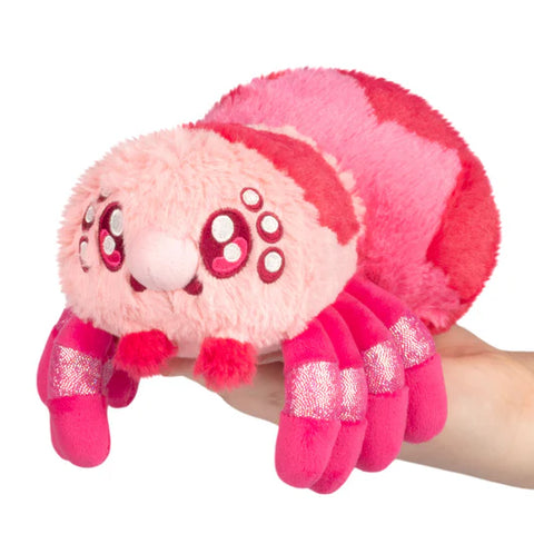 Plush toy resembling a pink spider held by a hand on a white background