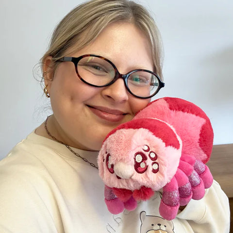 A woman holds the plush pink tarantula. It is slightly smaller than her head.