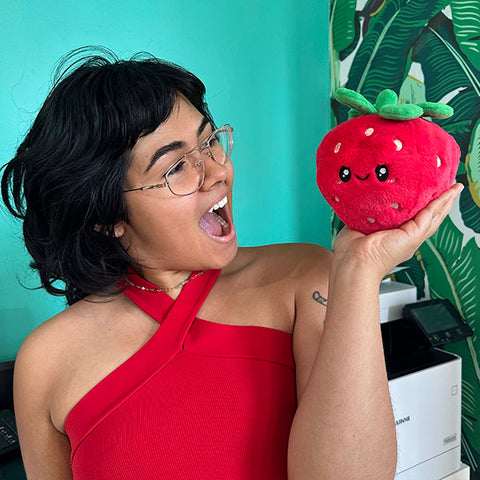 A woman holds the plush strawberry. It is slightly smaller than her head.