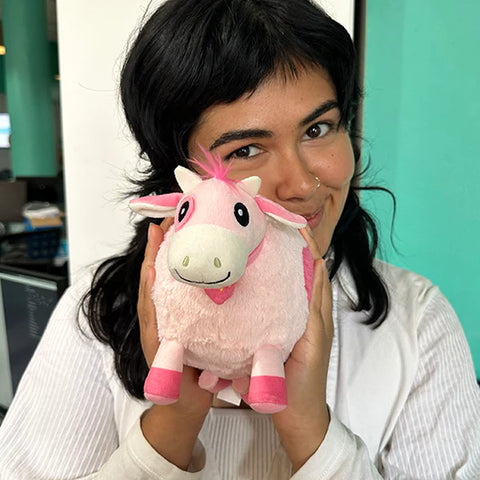 Image shows a woman holding the stuffed pink cow up to her face. It is slightly smaller than her head.