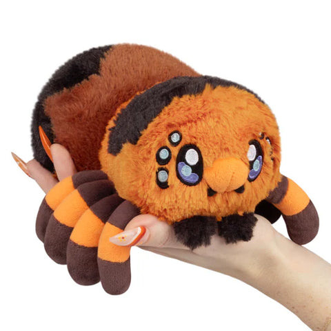 Image shows an orange, brown, and black stuffed tarantula being held in a woman's palm