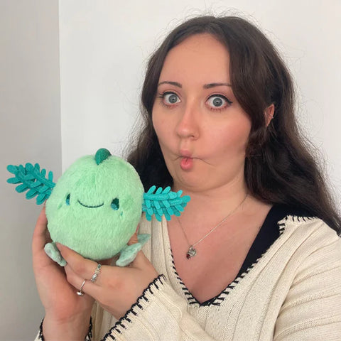 Image shows a woman holding the stuffed axolotl. It is about half the size of her head.