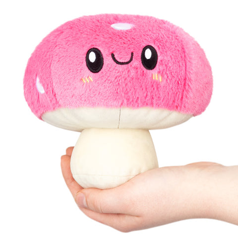 A plush toy resembling a pink mushroom with a smiling face, being held in a person's hand.